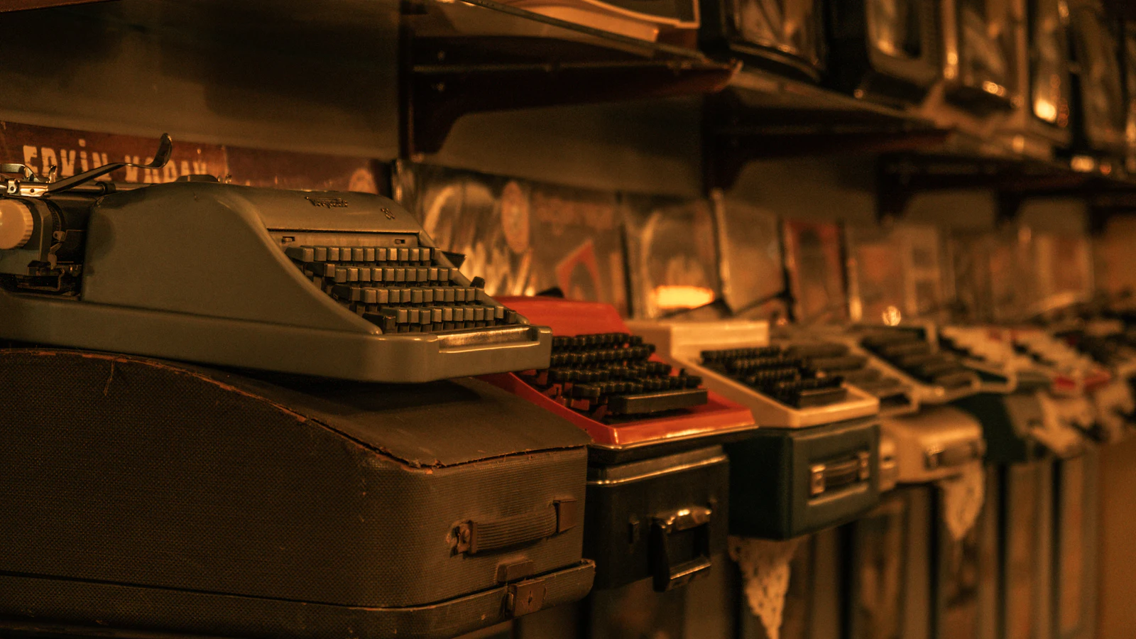 A row of old typewriters of different makes and colours on their cases in warm light, machines built for the same job that differ in how work goes in and comes out