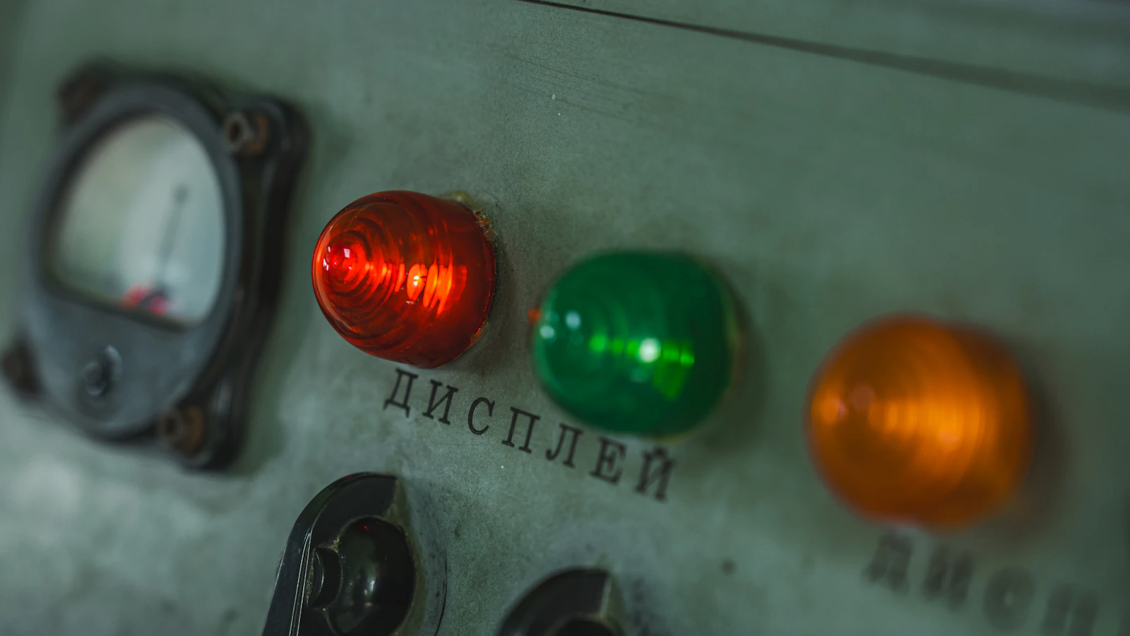A worn steel control panel with a lit red lamp beside a green and an amber one and an analogue meter, each lamp a single labelled fault that is either showing or clear