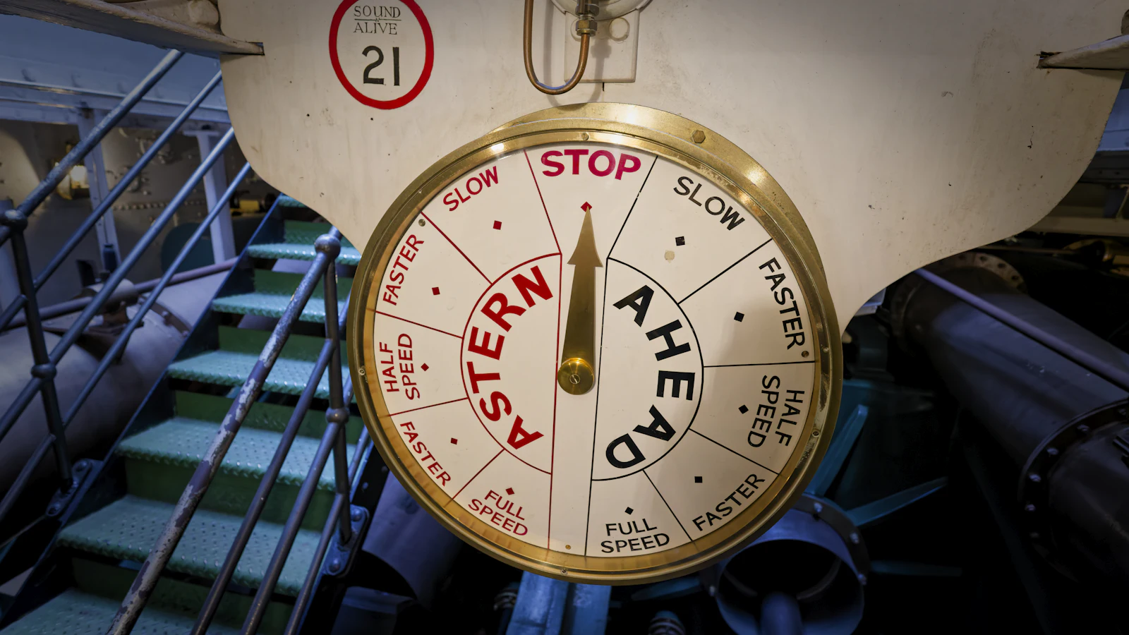 A brass engine order telegraph in a ship's engine room, its pointer at Stop between Ahead and Astern, where the bridge sends an order and the engine room carries it out, as delegated work changes hands