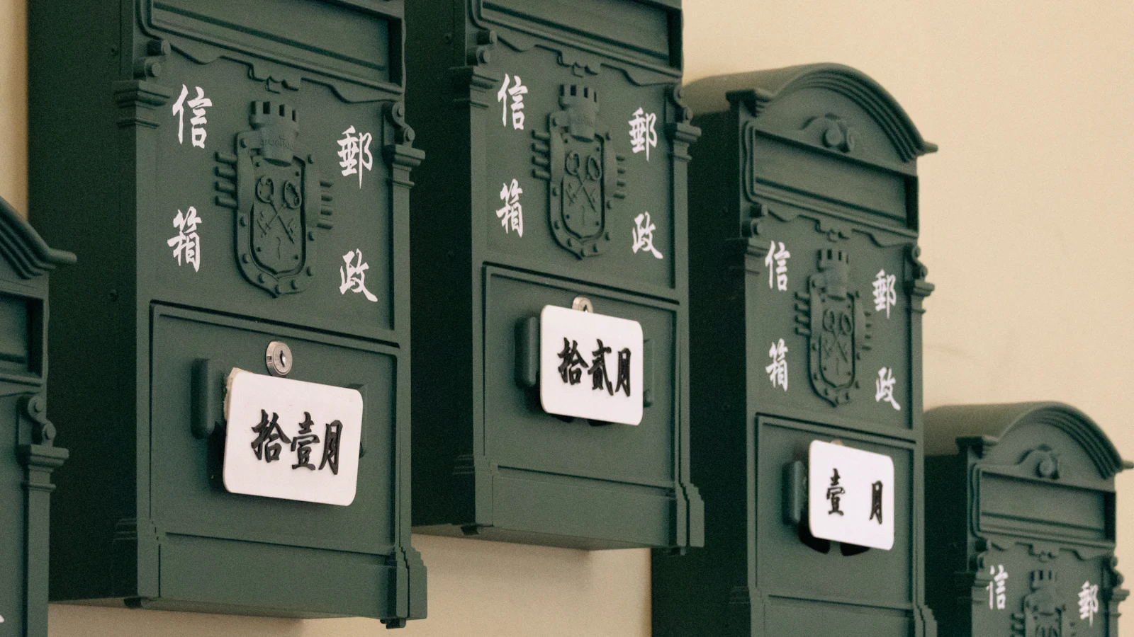 A row of identical green mailboxes on one wall, each with a white card naming a month in Chinese, one shared fixture with a slot for every box