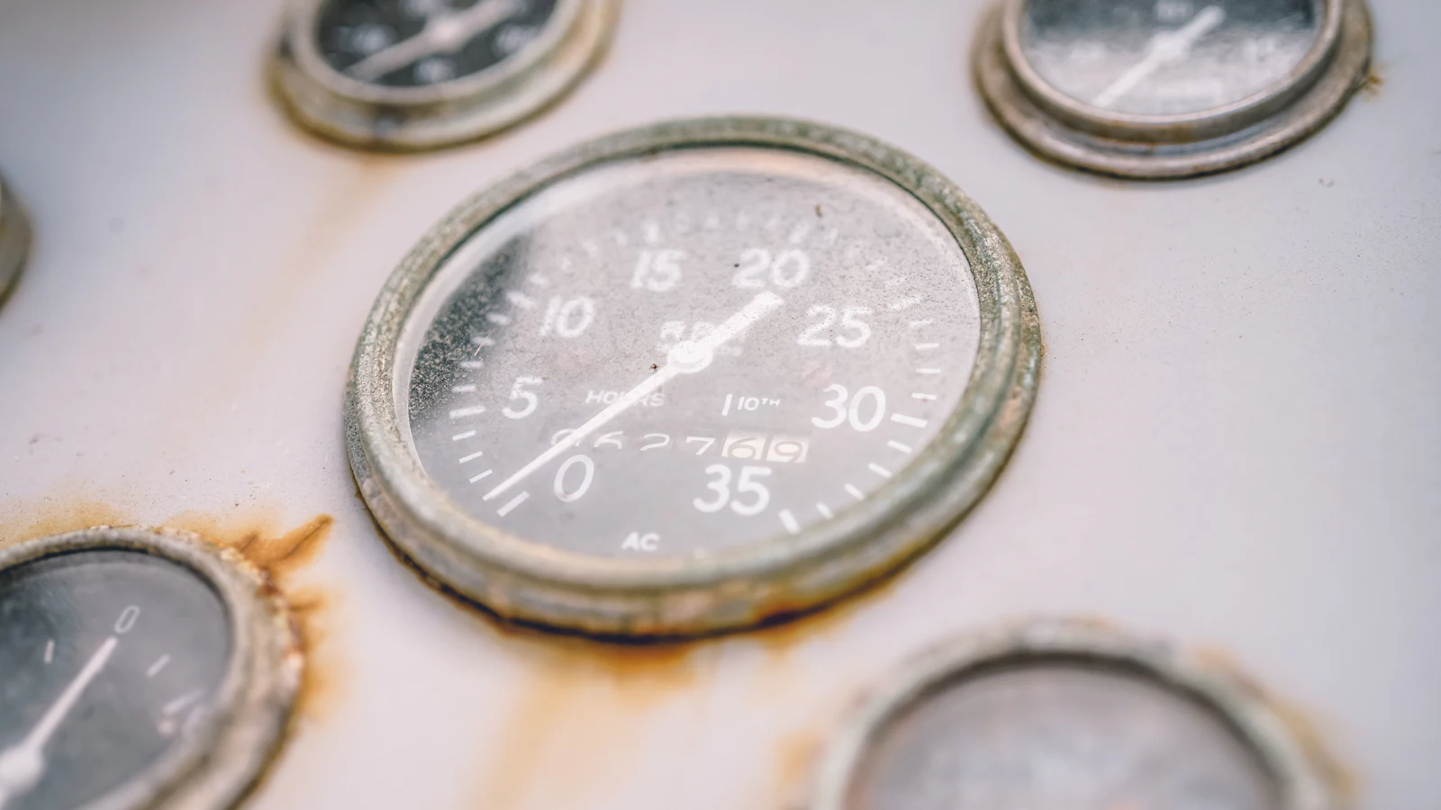 An hour meter in focus on a rust-streaked boat panel, counting how long the engine ran while the dials around it blur: a count of activity among the readings that could warn