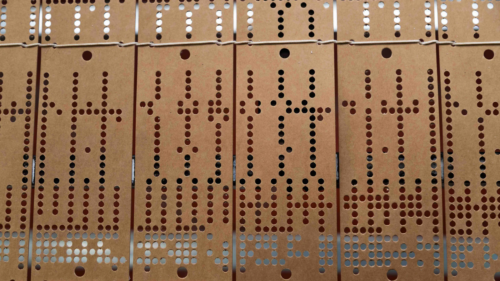 Brown punched cards laced together with string, each card holding the exact holes for one part of a larger pattern rather than the whole design