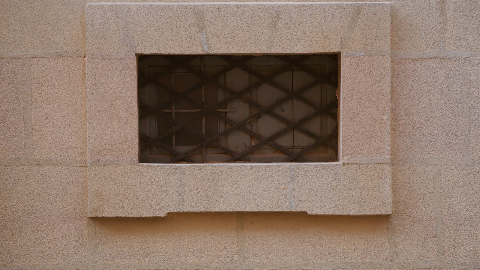 One small barred opening set into a wall of dressed stone, nearly all of it solid, the grille fixing exactly how much of what lies behind can be reached