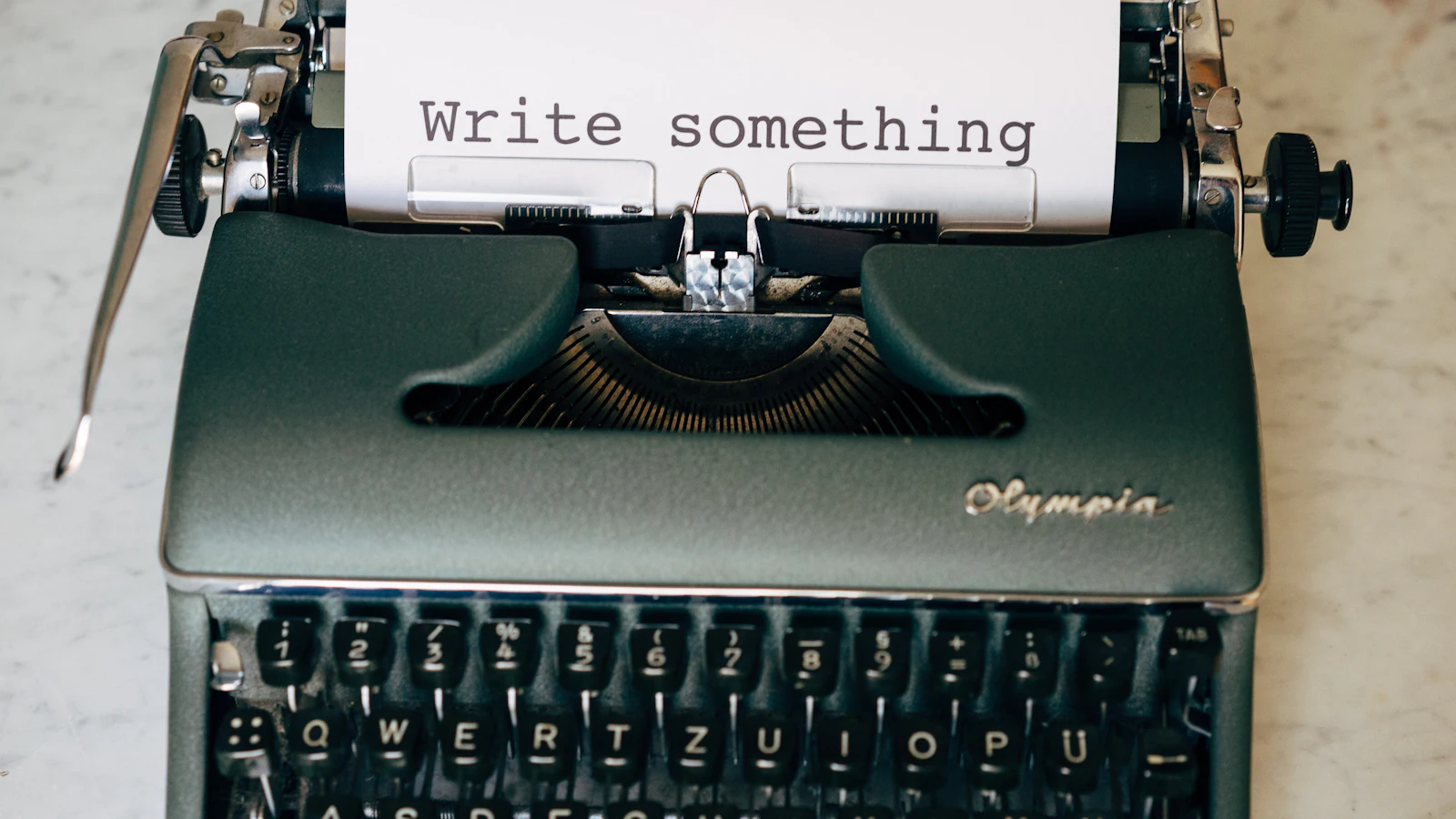 An Olympia typewriter holding a sheet that reads "Write something", an instruction that sets the form and leaves out the content, as the story template does