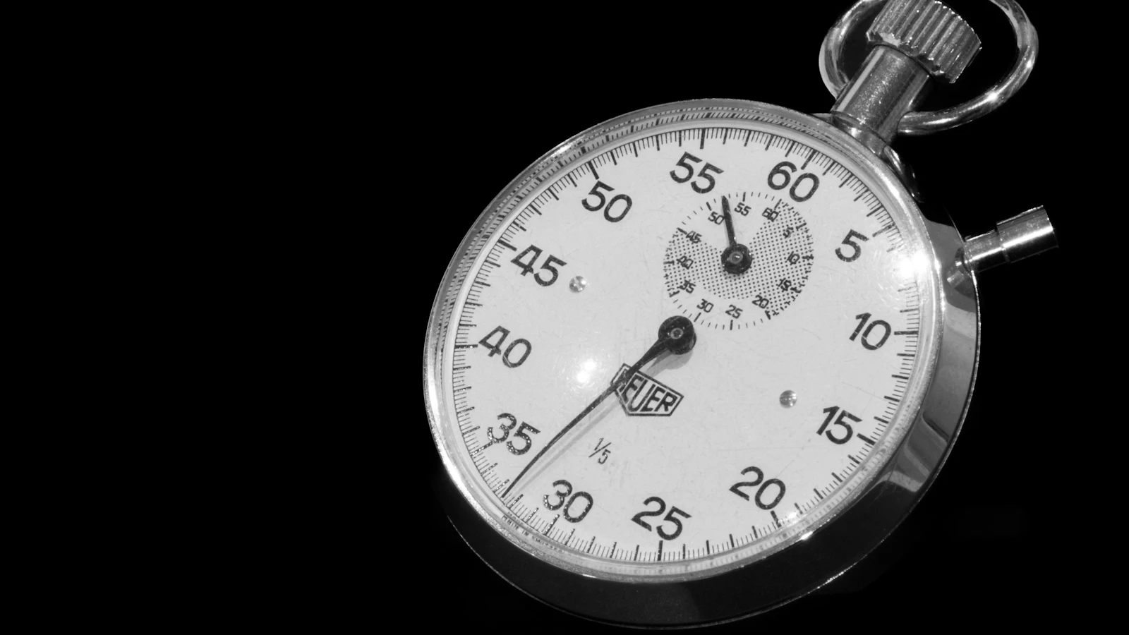 A mechanical stopwatch in black and white, its sweep hand timing the short interval while a small sub-dial counts the longer total on the same face