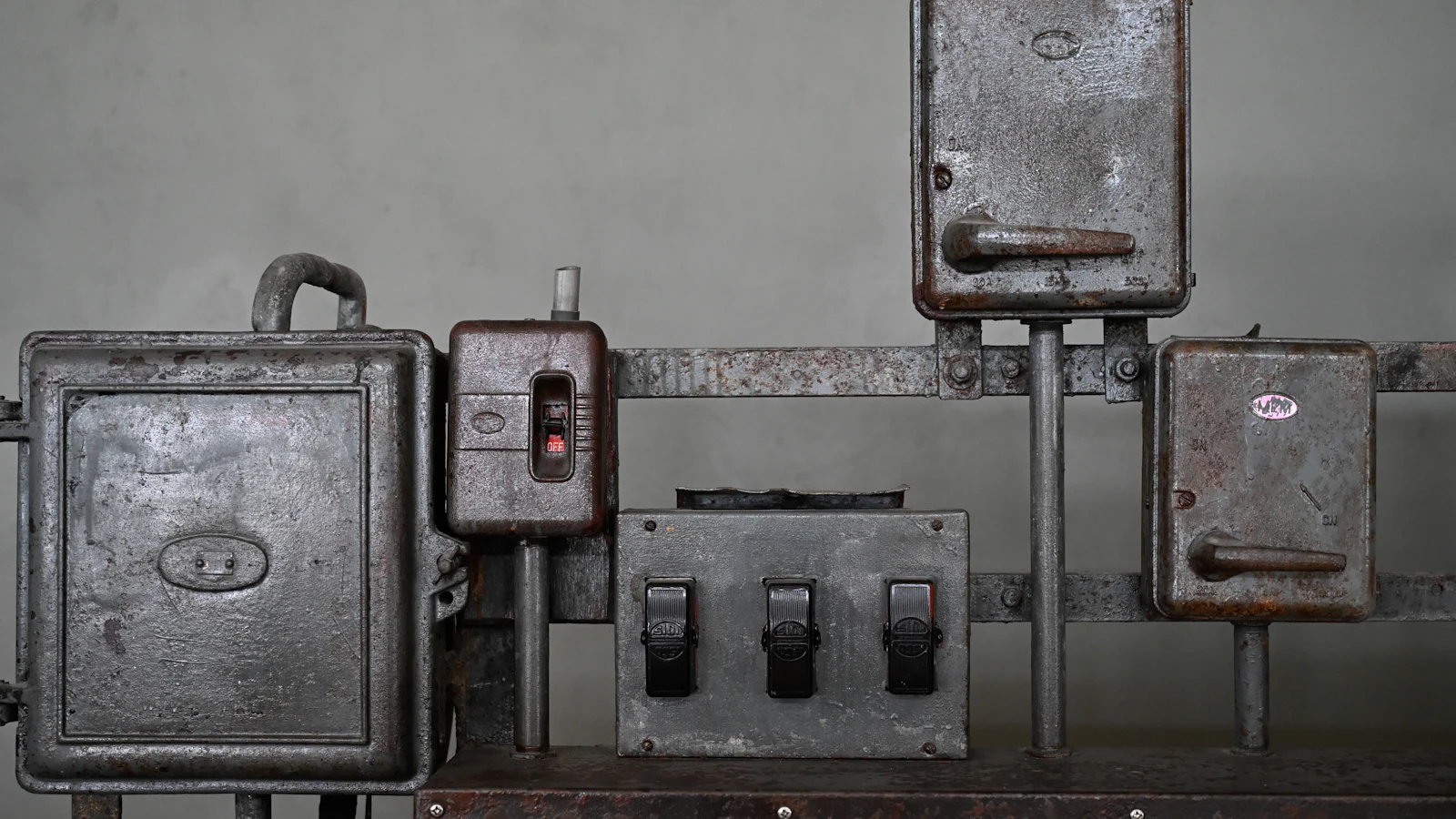 Old iron isolator switches and enclosures mounted on a rail, one window reading OFF and two with heavy handles, each box able to cut its own circuit