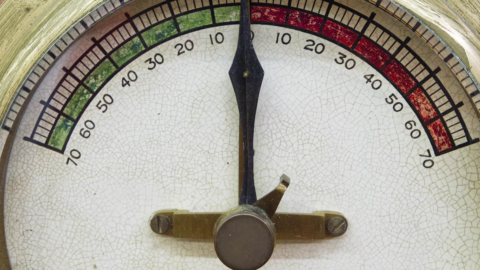 A crazed enamel dial whose scale runs to seventy on both sides of a central zero, green one way and red the other, the needle resting at zero