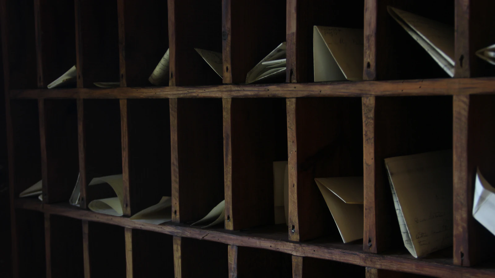 A dark wooden pigeonhole rack with folded letters sorted into some compartments and others left empty, each request either filed in its place or deliberately not taken