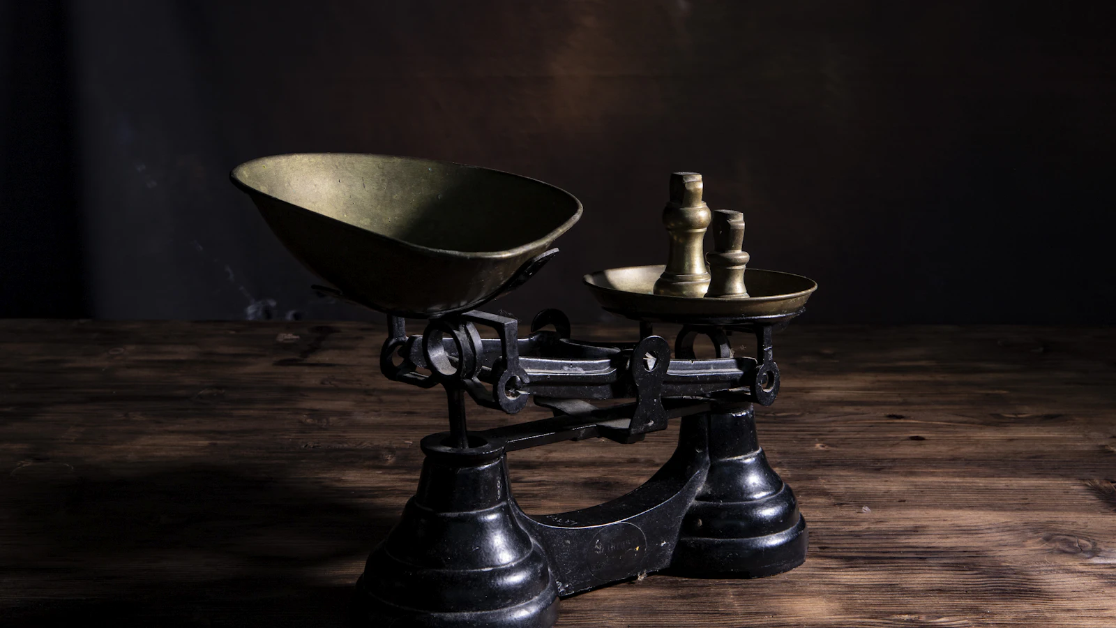 A cast-iron balance with an empty brass pan on one side and two brass weights on the other: every feature is weighed against what it displaces