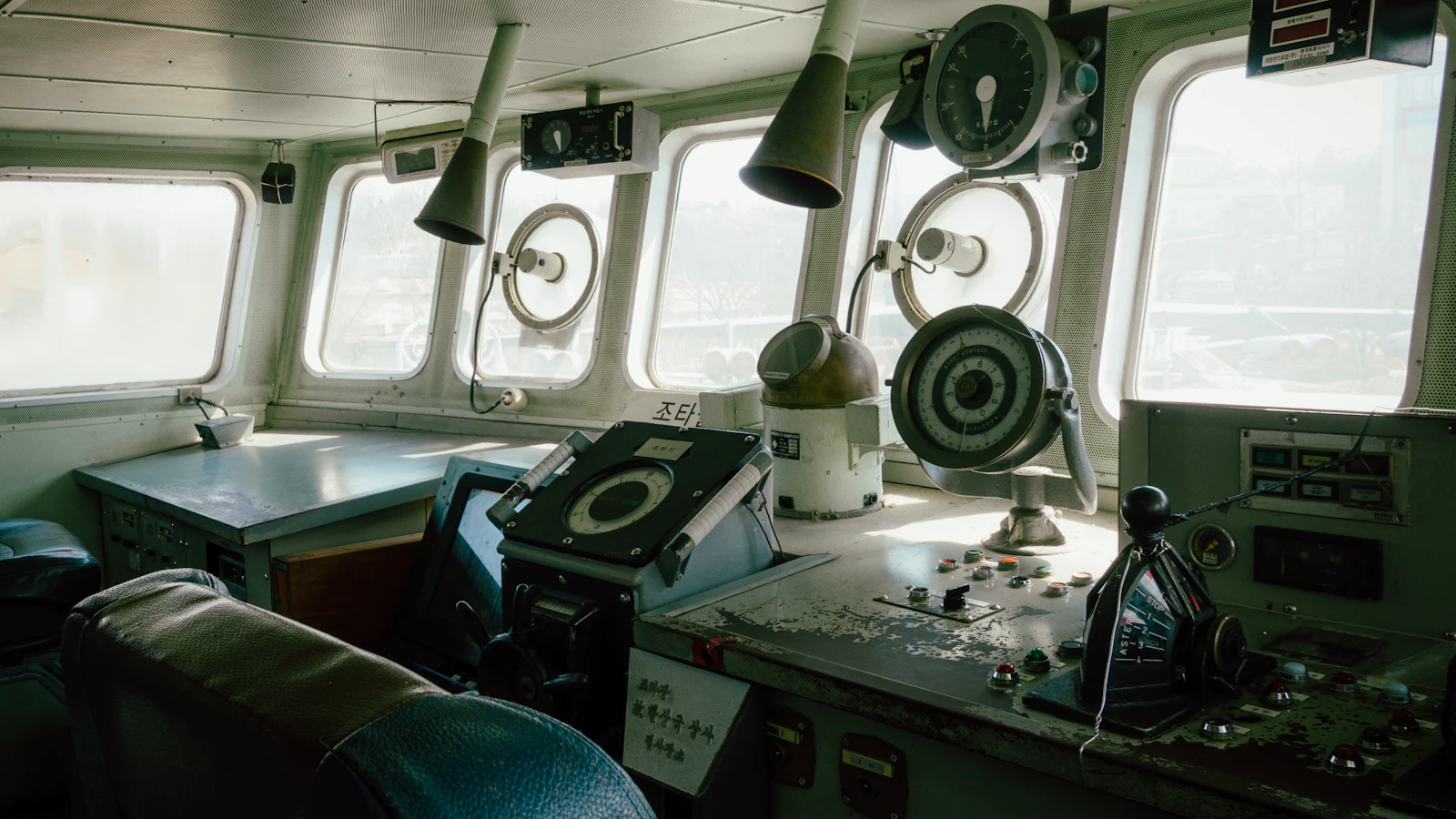 An empty ship's bridge with voice pipes, a steering stand and a round engine order telegraph, where the course is decided on one deck and the order carried to the people who execute it