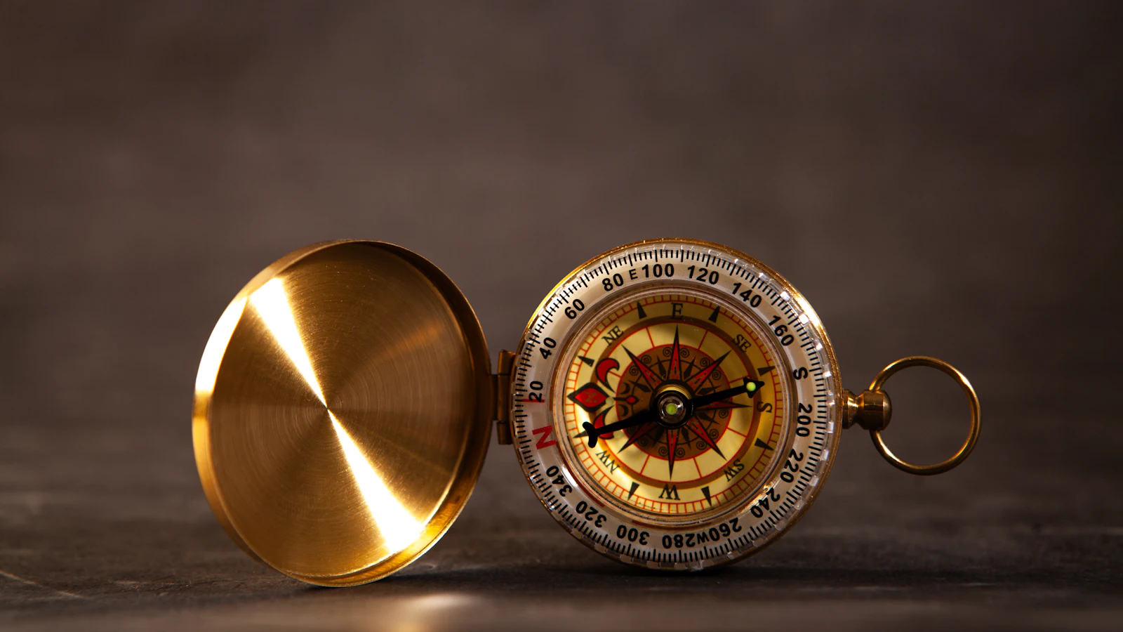 An open brass pocket compass on a dark surface, its needle holding one heading however the route below it changes, the way a sprint goal holds while the items change