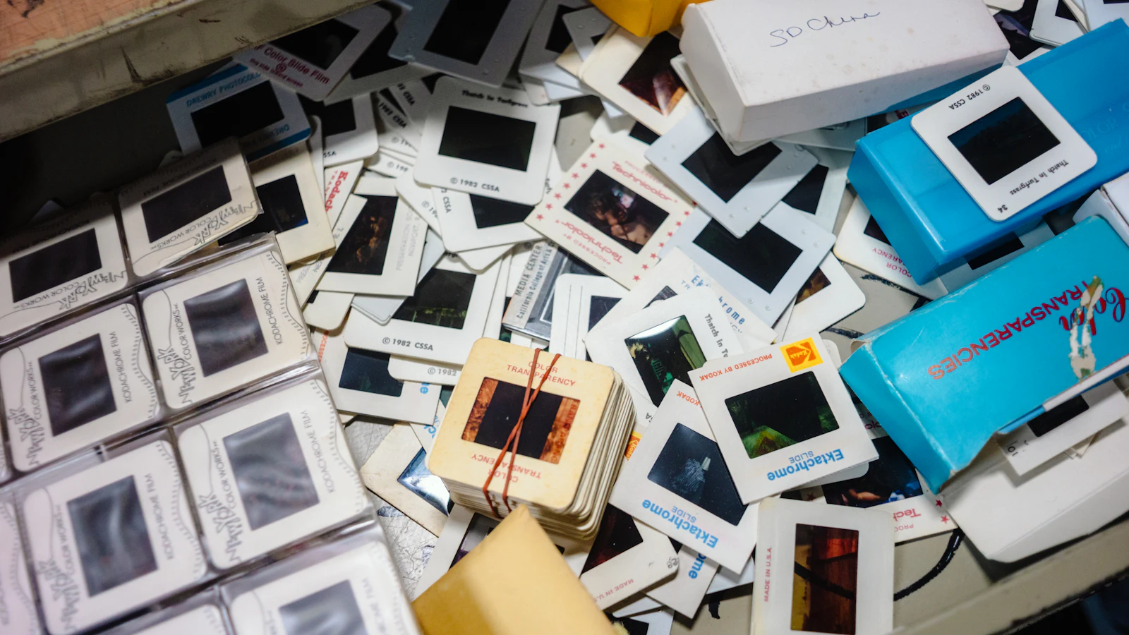 A drawer heaped with dozens of old photographic slides and their boxes, one small stack tied with a rubber band in the middle: far more than any audience could sit through, and the few picked out to show