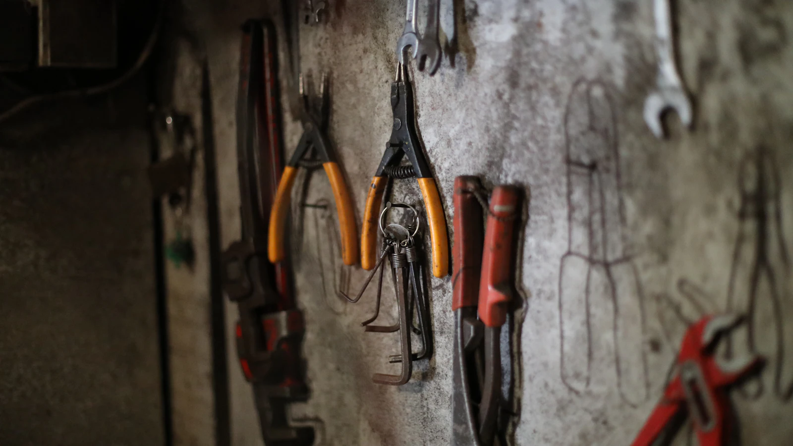 Pliers and wrenches hanging on a workshop wall beside outlines drawn where each tool belongs, some of them empty, a rule the whole bench agreed on and written so anyone can see when it is broken