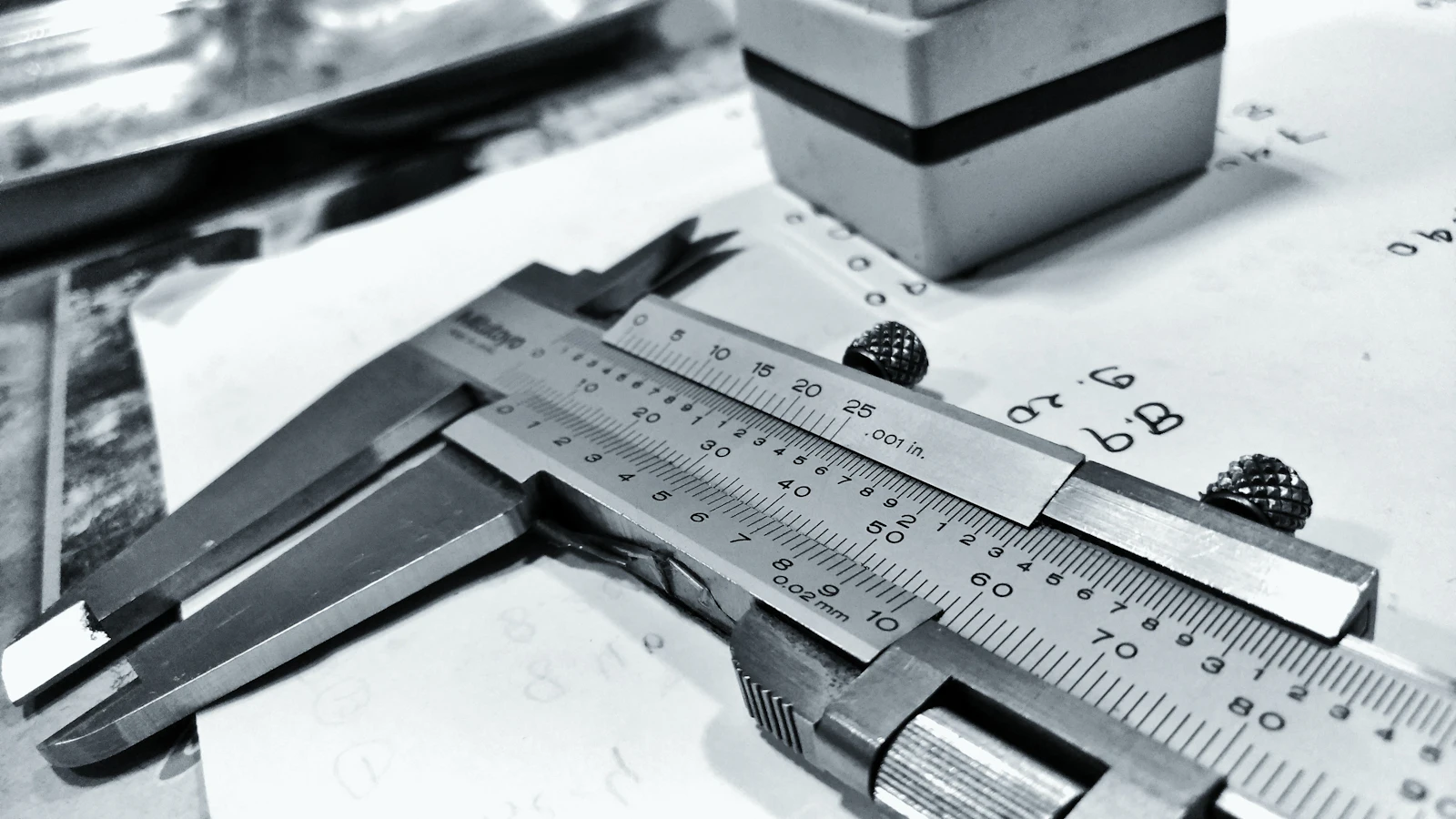 A steel vernier caliper lying on a sheet of handwritten measurements, its jaws and scale read against a known standard rather than against what the part was meant to be