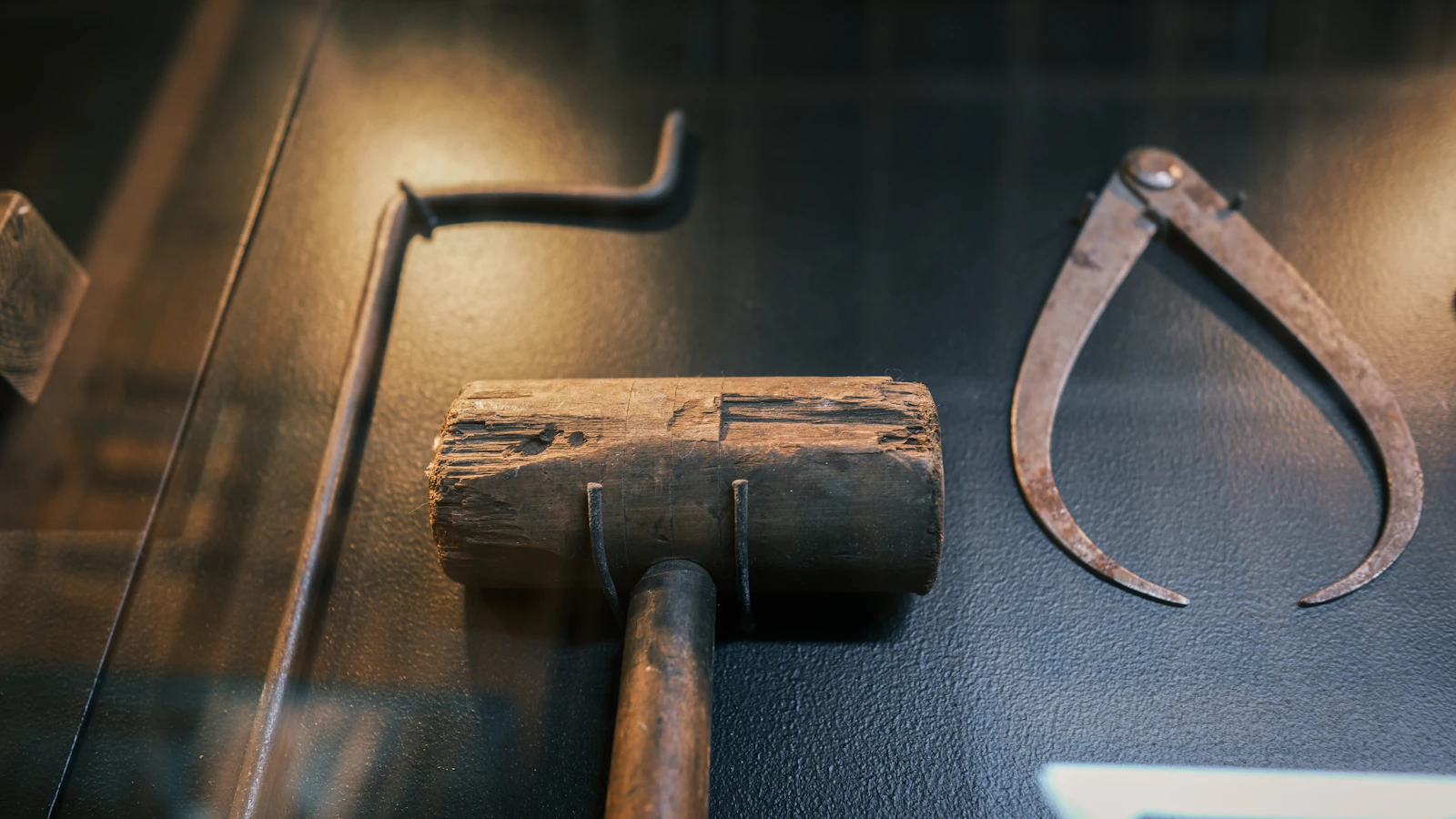 A worn wooden mallet beside a pair of iron calipers in a museum case: the tool that makes the work next to the tool that checks it, which is where a tech lead's hours move
