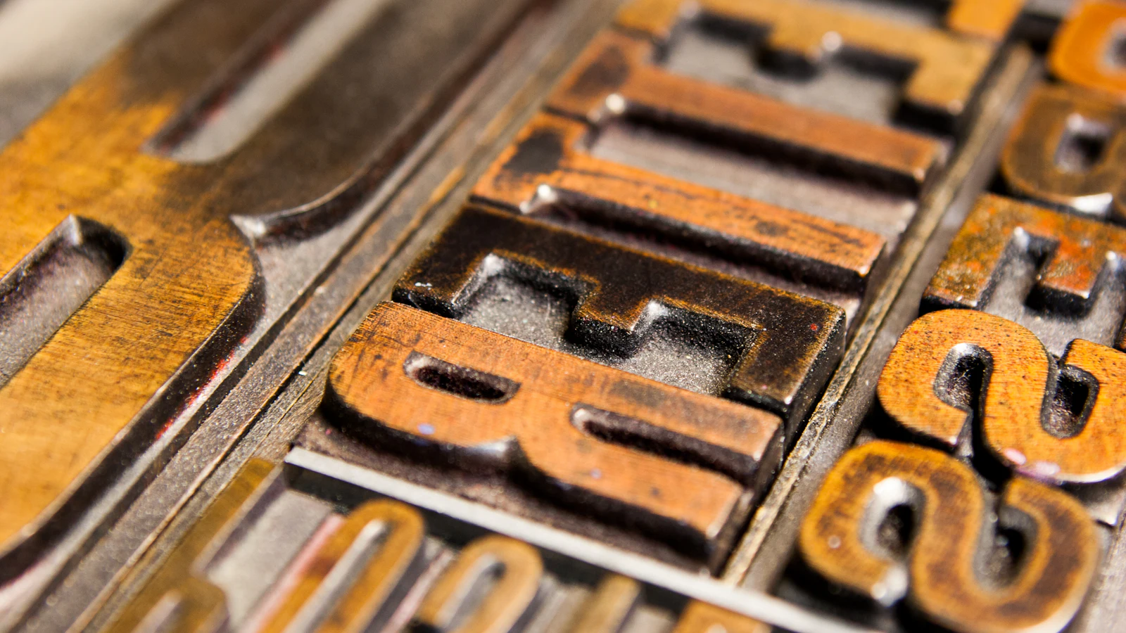 Inked letterpress type locked up in rows, the characters cut in mirror image — whatever is set into the frame is what every copy prints, faithfully and identically