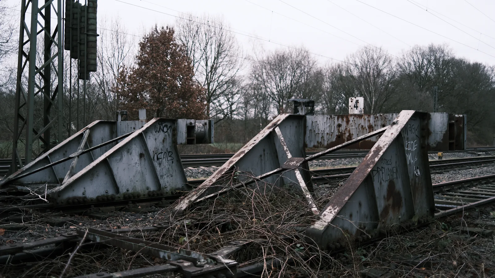 A row of rusted steel buffer stops at the ends of railway tracks on a grey day: the line ends here on purpose, and nothing is meant to go past it